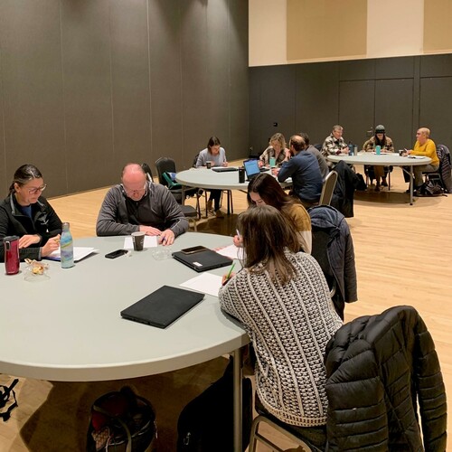 3 grey round tables have people seated around them.