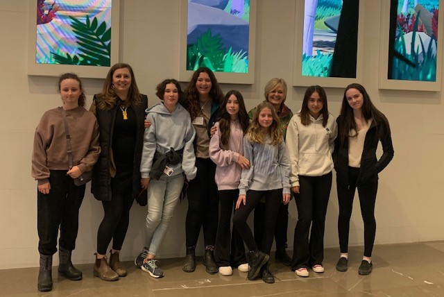 Seven students and two supervisors pose for a photo in front of four stained glass pictures.