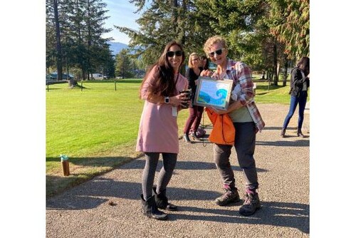 Two women posing with a certificate award outside. Grass and trees in the background