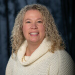 Middle aged woman smiling with blonde curly hair and beige sweater