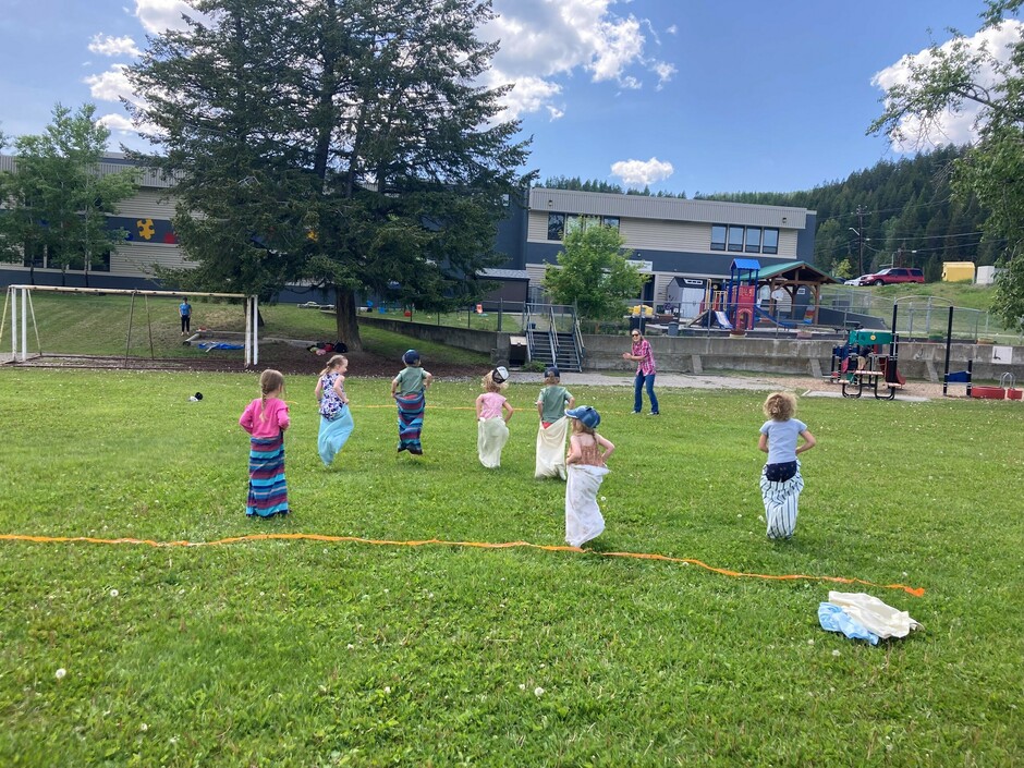 7 children are wearing a pillow case on their legs and racing.