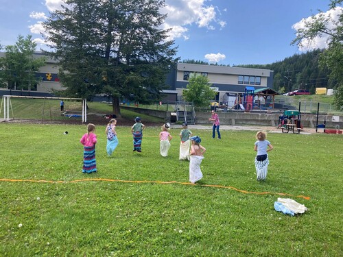Seven small children are wearing pillow cases on their legs as they race across grass to a finish line