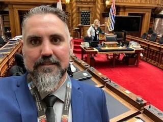 Middle-aged man taking a selfie with the Speaker's Chair and Clerks' table in the background