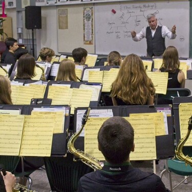 Music students facing a teacher providing instruction. Sheets of yellow music on stands