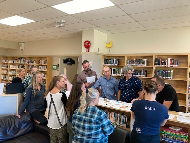 Eleven adults looking at samples of students work in a library